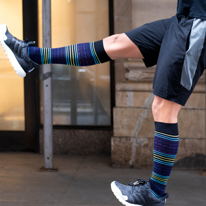 Compression socks with a colorful Aztec pattern, worn with black athletic shorts and shoes.