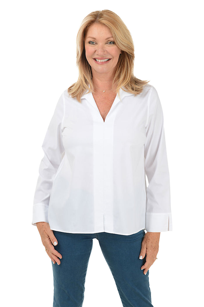 A front shot of a model wearing a white long sleeve blouse with a foldover collar, center front seam, and center back pleat. The blouse has long sleeves with 3-inch slits on cuffs and a high-low hemline with a 3-inch center slit.
