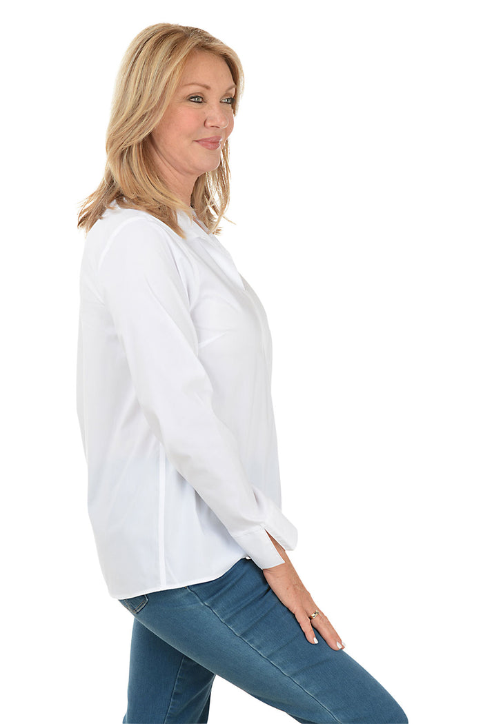 A side shot of a model wearing a white long sleeve blouse with a foldover collar, center front seam, and center back pleat. The blouse has long sleeves with 3-inch slits on cuffs and a high-low hemline with a 3-inch center slit.