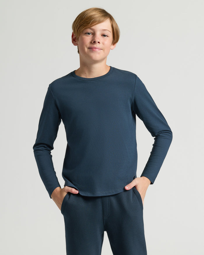 Boy wearing Boys' Navy Classic Long Sleeve Curved Hem Crew with hands in pockets.