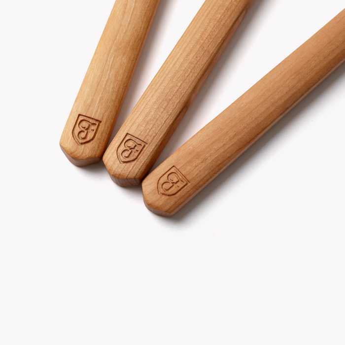 Close-up of three Field Cherry Wood utensil handles marked with the shield logo