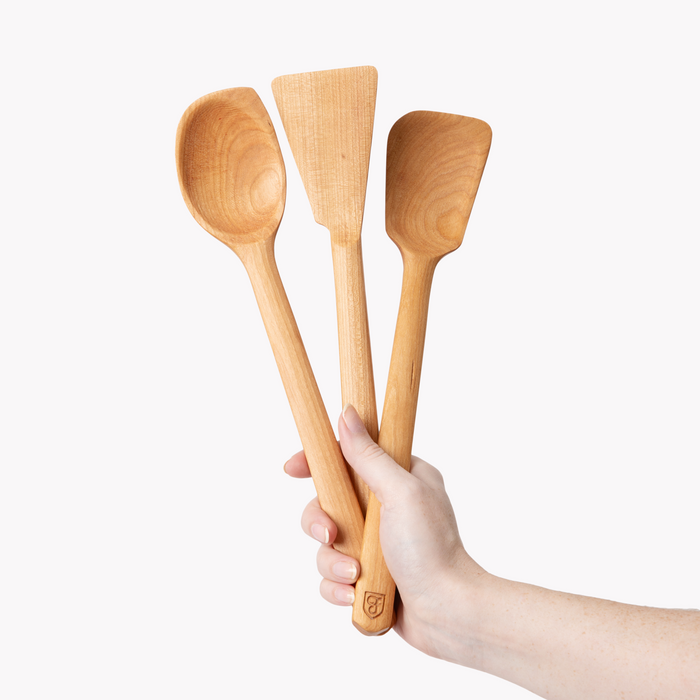 Hand holding the three Field cherry wood spoons and spatulas fanned out