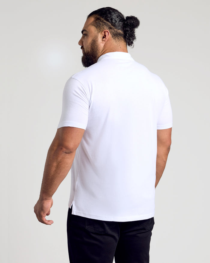 Man in White Classic Polo, dark trousers, hair in bun, facing away.