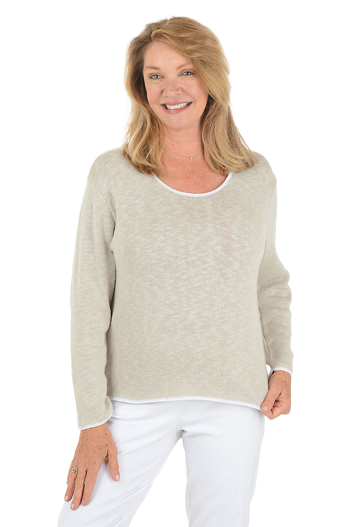 A woman wearing a scoop neck beige sweater with contrast white piping.