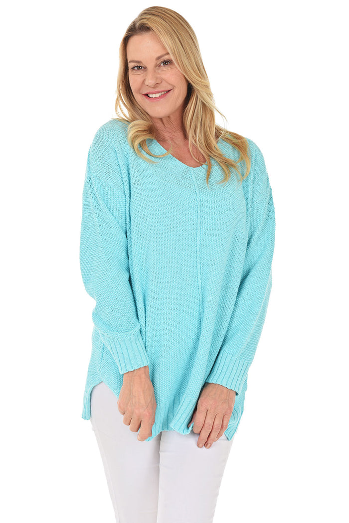 A woman wearing a long sleeve aqua cotton V-neck sweater, with a seam down the front and white pants.