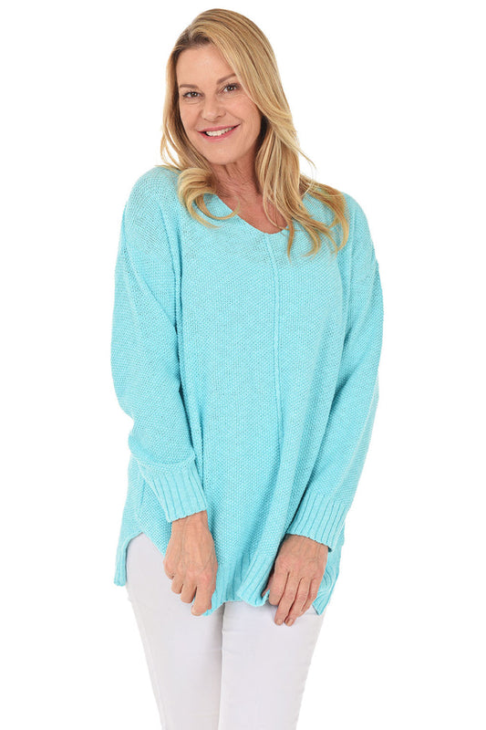 A woman wearing a long sleeve aqua cotton V-neck sweater, with a seam down the front and white pants.