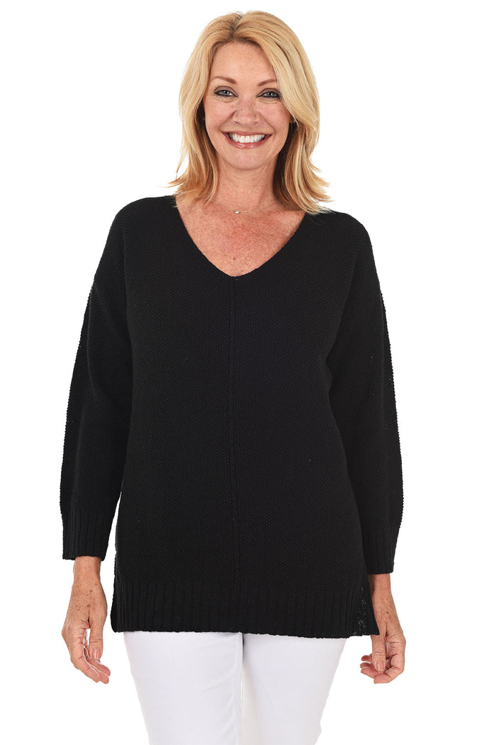 A woman wearing a long sleeve black cotton V-neck sweater, with a seam down the front and white pants.