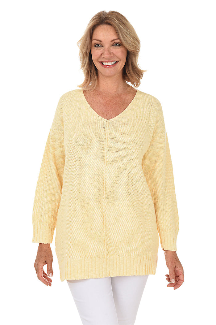 A woman wearing a long sleeve yellow cotton V-neck sweater, with a seam down the front and white pants.