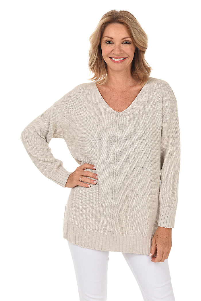 A woman wearing a long sleeve light grey cotton V-neck sweater, with a seam down the front and white pants.