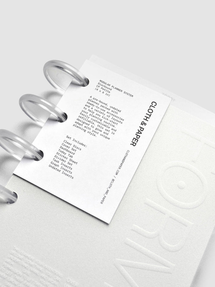 Close-up of a planner’s front tag label showing printed text describing an undated, customizable, refillable planner set with ready-to-use accessories and varied layouts.