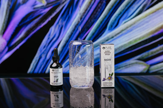 Night Water Infusion Drops | Pure Inventions bottle and box displayed next to a glass with infused water on a reflective surface with artistic blue and purple background, promoting skincare and wellness.