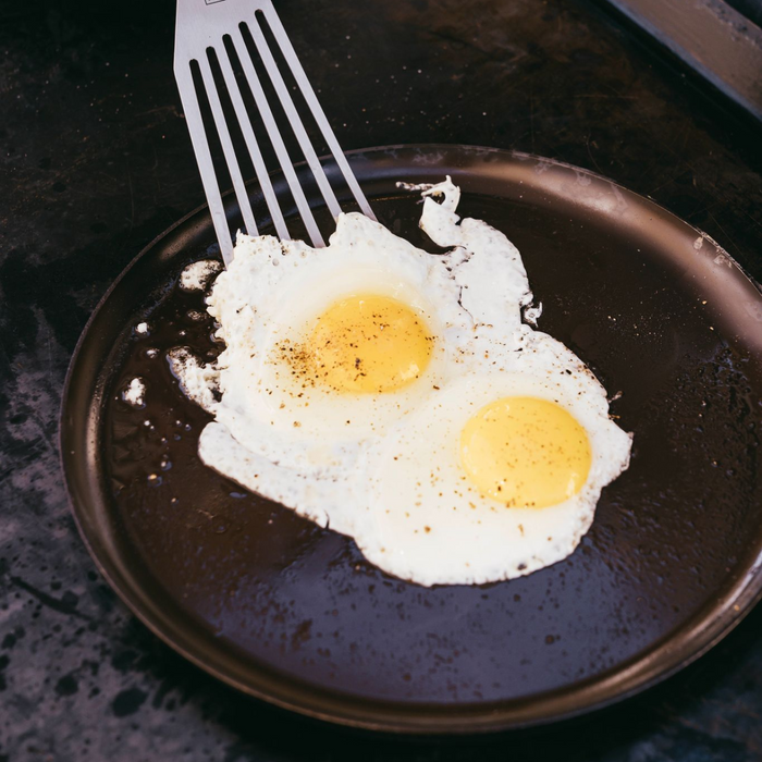 Two sunny-side-up eggs cooking on the No.9 Field Round Griddle, slotted turner easing under one