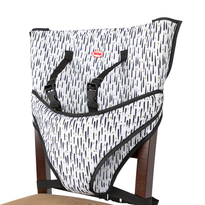 The Portable Toddler Travel Chair is a patterned fabric seat with black straps, buckles, and a five-point harness; it attaches securely to chairs with beige cushions for safe travel.