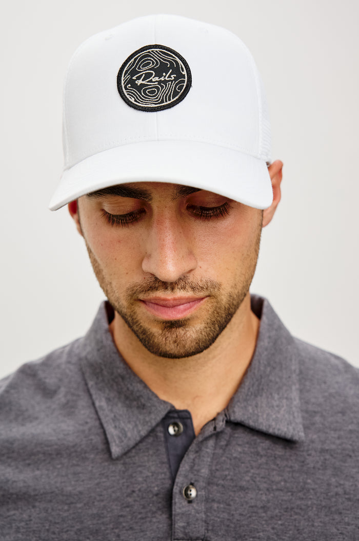 Golf Hat With Embroidered Branded Patch at Front, Adjustable Snapback, Mesh Back, and 6-Panel Construction in White Colorway - Upper Body Front View Featured on Model