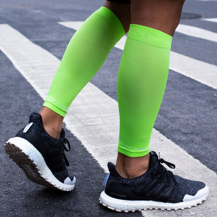Neon green compression calf sleeves worn with black athletic shoes on a crosswalk.
