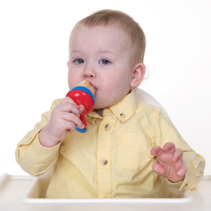 A baby in a yellow shirt sits in a high chair, holding the Nuby The Nibbler Feeder Replacement Net (3 pack) with squeeze and twist locking system, introducing whole foods against a plain white background.